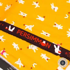 Nahaufnahme der Webkante Persimmon auf gelbem Baumwollstoff mit weißen Hasen