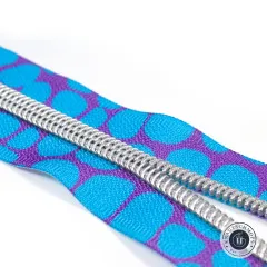 Diagonale Nahaufnahme der silberfarbenen Zähne auf dem blau-violett gepunkteten Zipper-Band vor weißem Hintergrund.