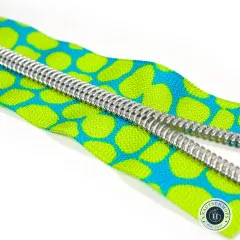 Diagonale Nahaufnahme der silberfarbenen Zähne auf dem lime-türkis gepunkteten Zipper-Band vor weißem Hintergrund.