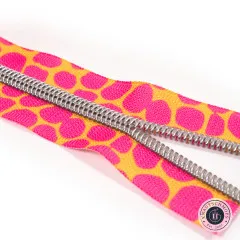 Diagonale Nahaufnahme der silberfarbenen Zähne auf dem pink-orangen gepunkteten Zipper-Band vor weißem Hintergrund.