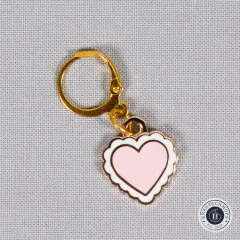 Detailaufnahme des Herz-Anhängers mit Karabinerhaken auf grauem Stoff.