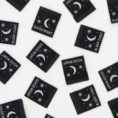 Weitere Nahaufnahme der schwarzen Weblabels mit weißem Mond- und Sternendesign, verstreut angeordnet.