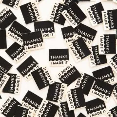 Dicht gestreute schwarze Sarah-Hearts-Weblabels „Thanks I Made It" mit weißem Siebdruck in wechselnden Ausrichtungen.