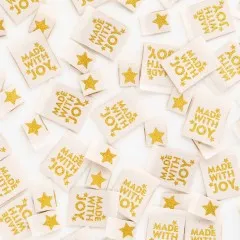 Dicht gestreute cremefarbene Sarah-Hearts-Weblabels „Made with Joy" mit goldenem Stern-Aufdruck in wechselnden Ausrichtungen.