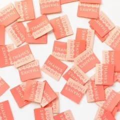 Dicht gestreute korallenfarbene Sarah-Hearts-Weblabels „Thanks I Made It" in Koralle und Creme, teils gedreht.