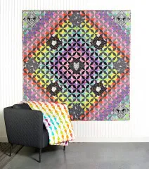 Cosmos-Variante des Dream Star Quilts in Regenbogenfarben, an der Wand hängend mit Galaxy-Decke im Vordergrund