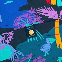 Label „Love You To The Moon and Back" eingenäht in einen bunten Stoff mit Pelikan- und Palmenmotiv.
