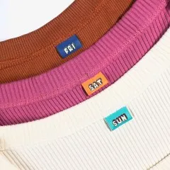 Die Label „Fri", „Sat" und „Sun" eingenäht in die Kragen dreier verschiedenfarbiger Nähprojekte.