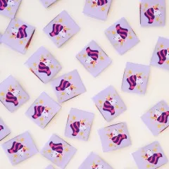Weitere Nahaufnahme der Einhorn-Weblabels mit rosa-violettem Mähnenmotiv und Goldakzenten.