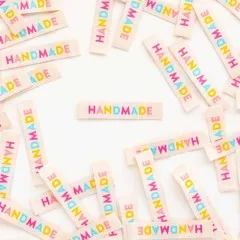 Ein cremefarbenes „HANDMADE"-Weblabel mittig platziert, umgeben von locker verstreuten weiteren Labels.
