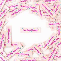 Ein cremefarbenes „Just Sew Happy"-Weblabel mittig platziert, umgeben von locker verstreuten weiteren Labels.