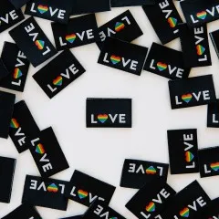 Ein schwarzes „LOVE"-Weblabel mit Regenbogenherz mittig platziert, umgeben von locker verstreuten weiteren Labels.