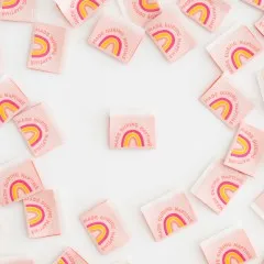 Ein rosafarbenes „Made during Naptime"-Weblabel mit Regenbogenmotiv mittig platziert, umgeben von locker verstreuten weiteren Labels.
