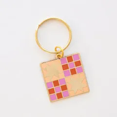 Schlüsselanhänger mit Quilt-Sternmuster in Rosa, Orange und Gold vor weißem Hintergrund.