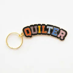 Schlüsselanhänger mit dem Schriftzug „Quilter“ in bunten Mustern vor weißem Hintergrund.