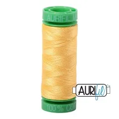 Aurifil-Garnrolle mit grünen Endkappen, bespult mit blassgelbem Baumwollgarn, freigestellt vor weißem Hintergrund.