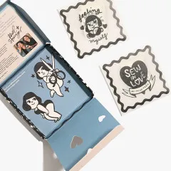 Die geöffnete Box zeigt im Deckel eine bedruckte blaue Innenseite mit Illustrationen, daneben liegen zwei einzeln in Wellenrand-Folie verpackte Labels „feeling myself“ und „Sew in Love“.