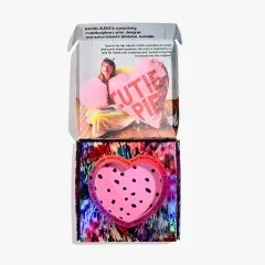 Geöffnete Box mit gepunktetem Herz-Ausschnitt und Foto von Rachel Burke mit „Cutie Pie"-Kissenherz im Deckel.