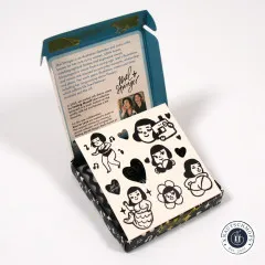 Die geöffnete Box zeigt im Deckel den Info-Text über Künstlerin Mel Stringer, davor liegt ein perforierter Bogen mit den noch ungetrennten Label-Illustrationen wie Meerjungfrau, Blume und tanzender Figur.