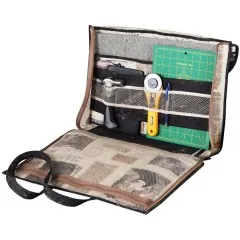Geöffnete Portfolio-Tasche in dunklem Zeitungsdruck-Design mit Schneidematte, Rollschneider und Werkzeugen.