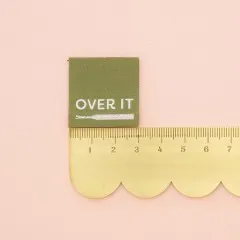 „Over It“-Label neben einem goldenen Lineal zum Größenvergleich.