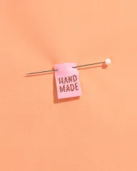Rosa 'Hand Made'-Label mit Stecknadel auf pfirsichfarbenem Stoff