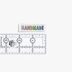 Einzelnes Handmade-Label in Regenbogenfarben neben einem Lineal zur Größeneinordnung