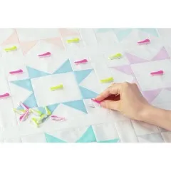 Wonder Pins in Pink und Gelb auf einem hellen Patchwork-Quiltblock, eine Hand setzt eine weitere Nadel