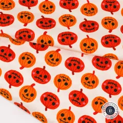 Nahaufnahme des Kürbis-Stoffs mit gefalteter Stoffkante, orange-rote Jack-O-Lantern-Gesichter auf Creme