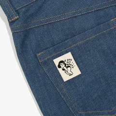 Das Label „It fits my booty“ ist auf die Gesäßtasche einer blauen Jeans genäht, Nahaufnahme der Denim-Textur mit oranger Ziernaht.