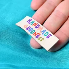 Bunt besticktes 'Handmade Goodness'-Label in der Hand auf türkisfarbenem Stoff
