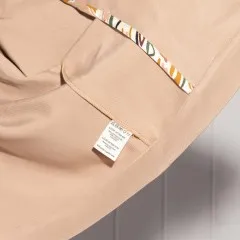 Eingenähtes Label in der Tasche eines beigen Kleidungsstücks mit gemustertem Besatz