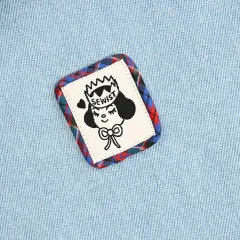 Das Label „Sewist“ mit Krone ist auf hellblauen Denimstoff genäht und von einem karierten Flanell-Stoffflicken umrandet.