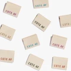 Zahlreiche Cute-AF-Label in Rosa, Türkis, Khaki und Roségold aus der Vogelperspektive drapiert.