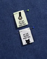 Zwei Labels mit Stecknadeln auf blauem Jeansstoff befestigt.