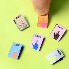 Lose Labels in verschiedenen Farben auf grünem Stoff, eines wird zwischen zwei Fingern gehalten.