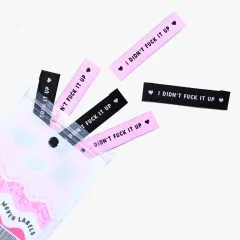 Labels 'I Didn't Fuck It Up' in Schwarz und Rosa beim Herausfallen aus der Verpackung.
