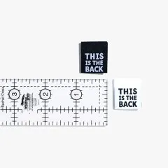 Ein schwarzes und ein weißes Label 'This is The Back' neben einem Patchwork-Lineal zum Größenvergleich