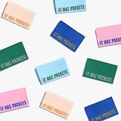 Mehrere bunte Labels 'It Has Pockets' verstreut in der Draufsicht.