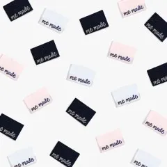 Mehrere Metallic-Labels 'me made' in drei Farben verstreut in der Draufsicht.