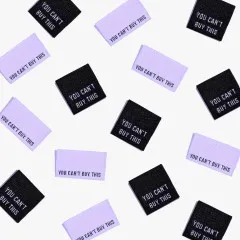 Mehrere Metallic-Labels 'You Can't Buy This' in Lila und Schwarz verstreut in der Draufsicht.