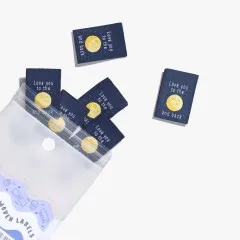 Mehrere „Love You To The Moon and Back"-Labels lose verstreut, teils aus der geöffneten Verpackung ragend.