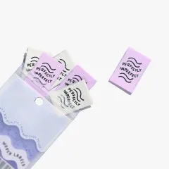 Mehrere „Perfectly Imperfect"-Labels in Elfenbein und Flieder lose verstreut, teils aus der geöffneten Verpackung ragend.