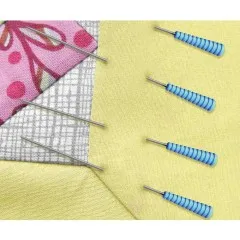 Blaue Magic Pins Quilting stecken in einem rosa-grauen Patchwork-Eckstück auf gelbem Stoff.
