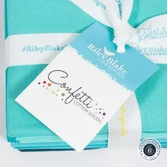 Nahaufnahme des rautenförmigen Anhängers „Confetti Cotton Solids“ von Riley Blake Designs auf dem türkisfarbenen Stoffbündel mit weißem Hashtag-Band