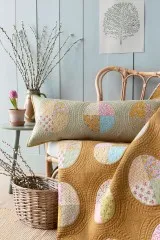 Patchwork-Quilt und -Kissen mit rundem Medaillon-Muster aus der Spring-Kollektion auf einem Rattanstuhl.