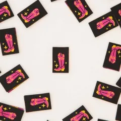 Schwarze Weblabels mit pinkfarbenem Cowboystiefel und goldenen Glitzersternen verstreut auf hellem Untergrund.