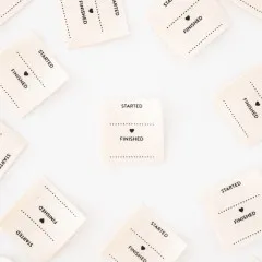 Nahaufnahme mehrerer „Started/Finished"-Weblabels mit Herzsymbol, verstreut auf weißem Untergrund.