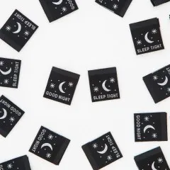 Nahaufnahme mehrerer „Good Night"- und „Sleep Tight"-Weblabels mit Mond- und Sternenmotiv, locker verstreut.