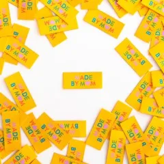 Mehrere gelbe Weblabels "Made by Mom" mit buntem Text im Kreis um ein einzelnes zentrales Label angeordnet.